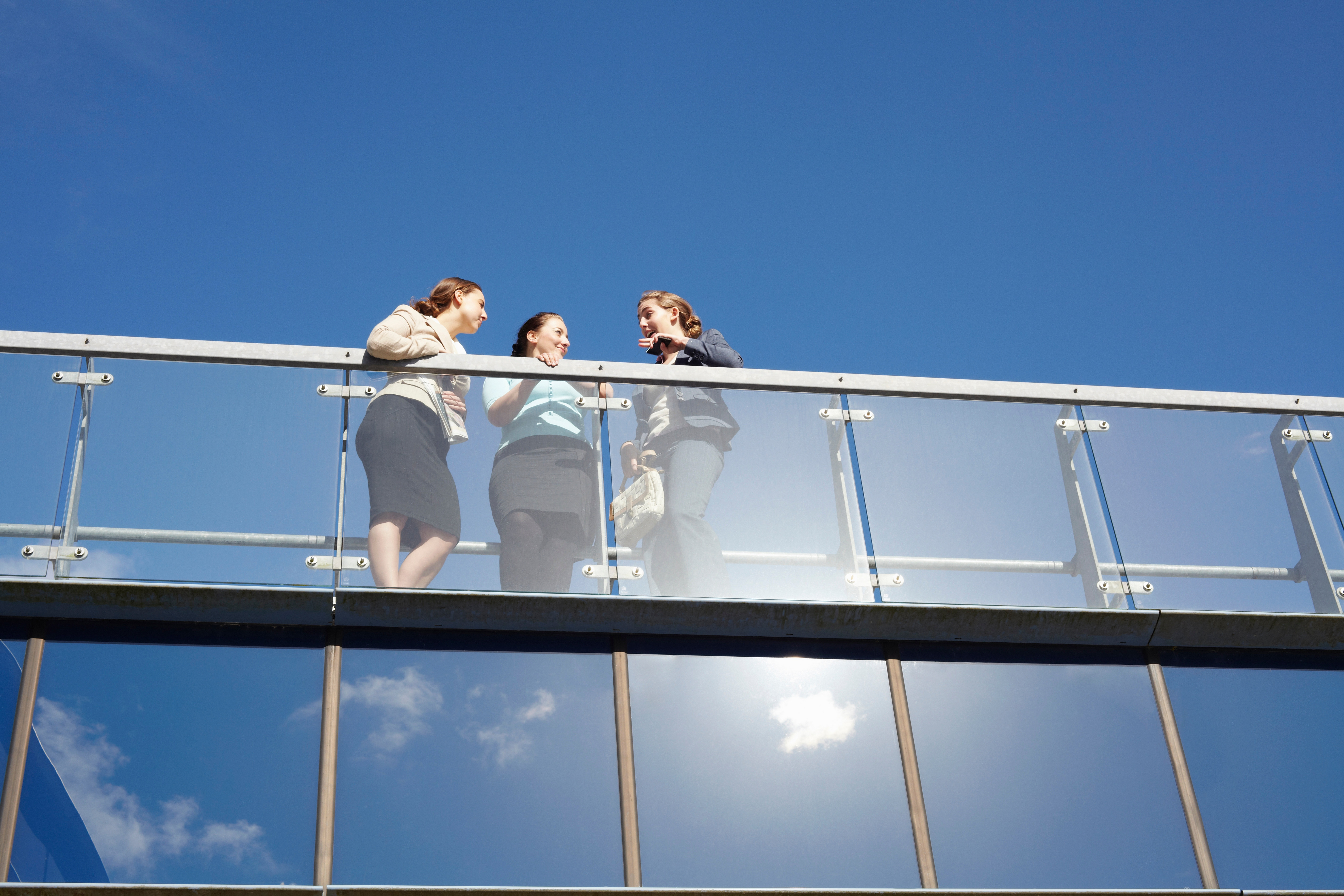 Three women enjoy the view from a balcony fenced by glass railings